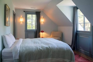 A bedroom with a bed, two bedside lamps, a chair, and a window.