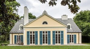 A two-story house with a gabled roof, a chimney, and a front porch with a chair. - Colle | Historic Estate with Pool (Charlottesville)