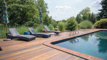 Une terrasse en bois avec des chaises longues et des parasols, une piscine et une végétation luxuriante tout autour.