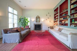 A living room with two sofas, a red rug, a fireplace, and a bookshelf.