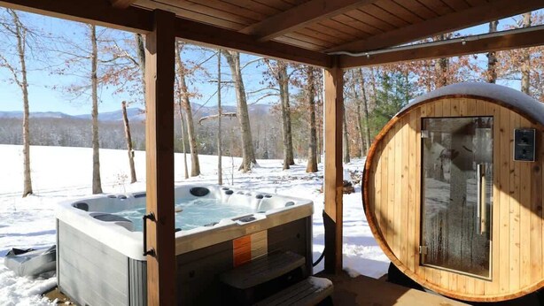 Eine Holzhütte mit Whirlpool und Sauna, umgeben von Schnee und Bäumen.