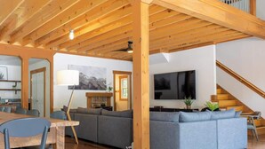 Ein geräumiger Wohnbereich mit Holzbalkendecke, einem großen grauen Sofa, einem Flachbildfernseher und einer Treppe.