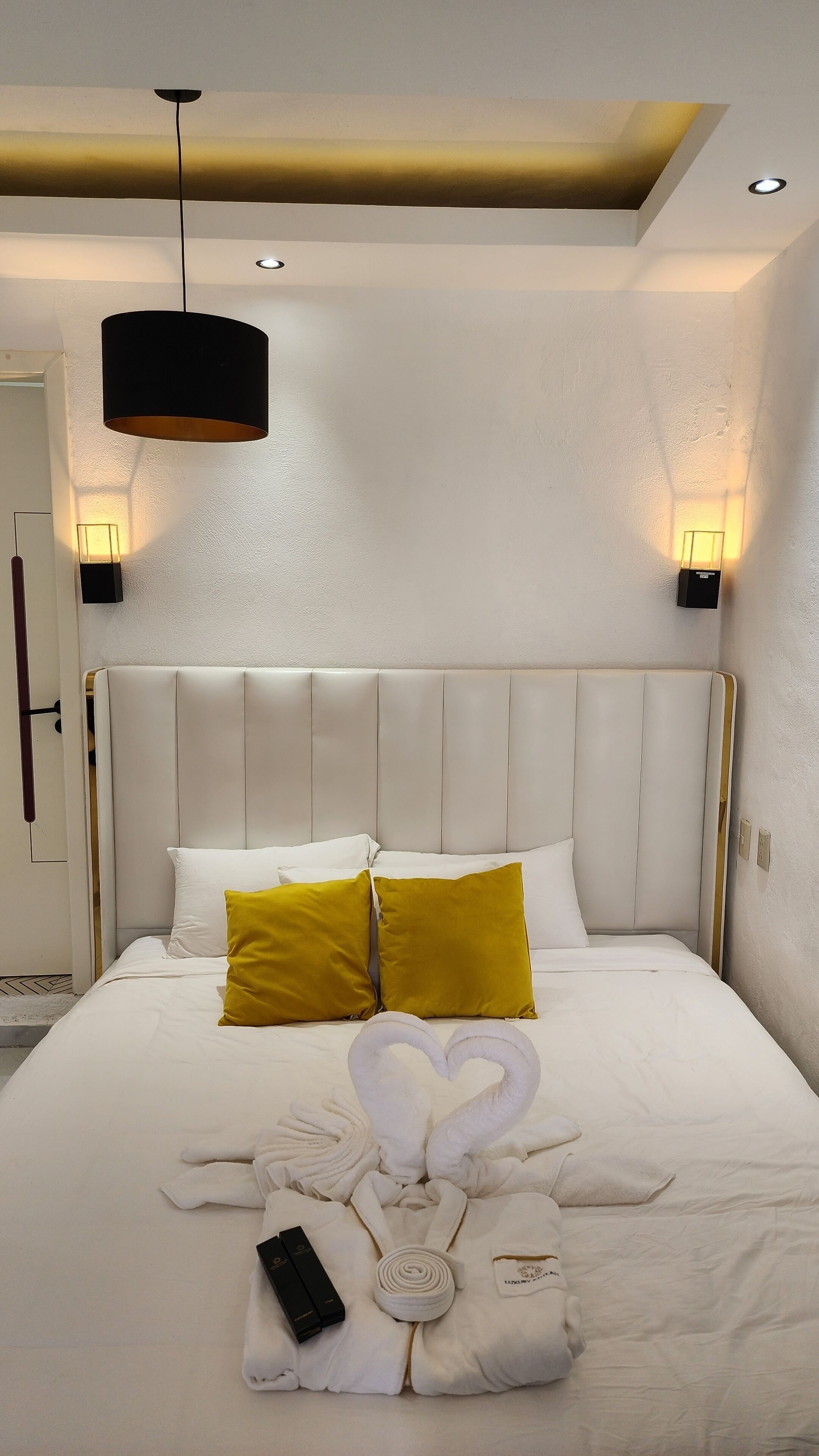 Camera d'albergo con un grande letto, due luci a parete, una luce a soffitto e un letto rifatto con asciugamani e telecomando.