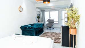 Un dormitorio moderno con una cama grande, un sofá de terciopelo azul, una silla negra y una planta en maceta.