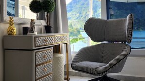 Una habitación moderna con un gran ventanal, un escritorio con cajones, una silla y una planta en maceta.