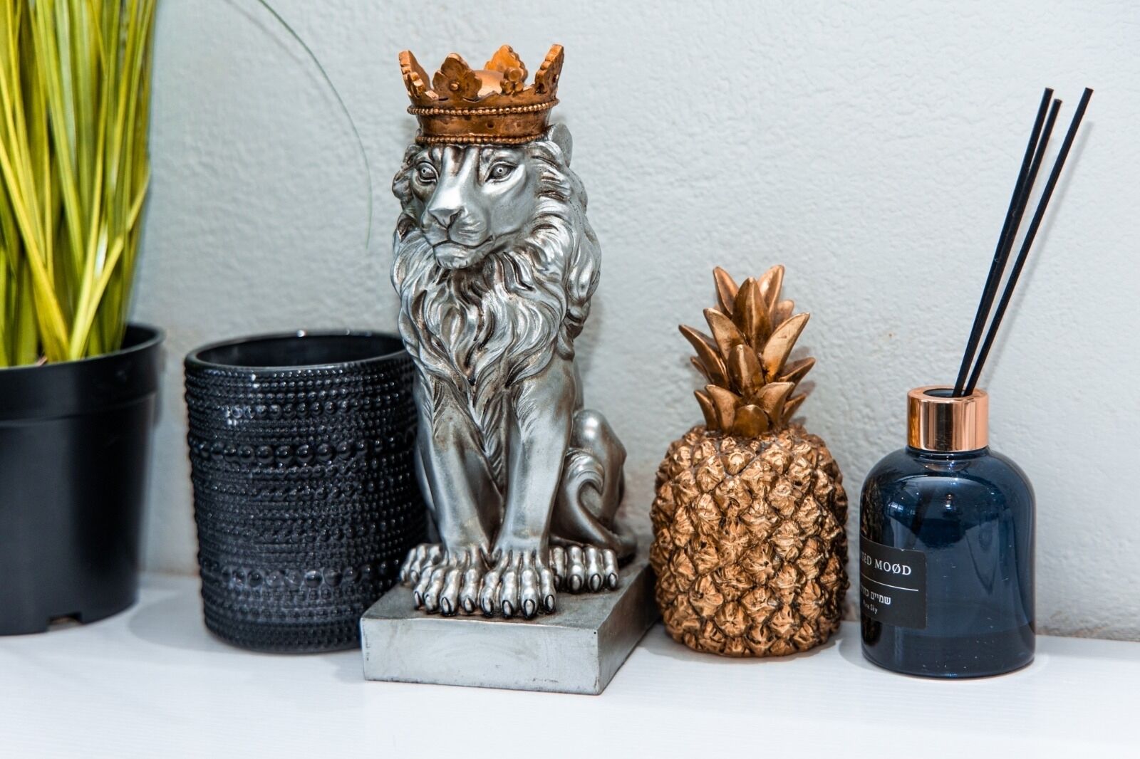 Une statue de lion décorative, surmontée d’une couronne, un porte-bougie en forme d’ananas, un vase noir texturé et un porte-bougie bleu avec des mèches noires.