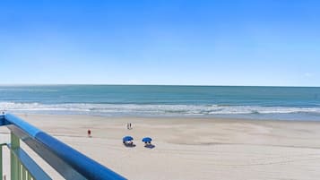 Vista a la playa desde un balcón con barandilla, una playa de arena y el océano.