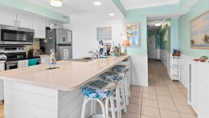 Una cucina con mobili bianchi, una grande isola con sgabelli da bar, un forno a microonde e un frigorifero.