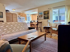 A living room with a sofa, coffee table, and chairs, a kitchen in the background, and a dining area with a table and chairs. - Peaceful, Fully Equipped Cabin Near Beach & Town, Certified NWF Wildlife Habitat (Seaview)