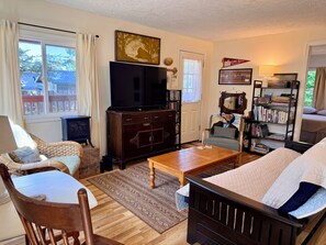 A cozy living room with a television, bookshelves, a comfortable sofa, and a dining table. - Peaceful, Fully Equipped Cabin Near Beach & Town, Certified NWF Wildlife Habitat (Seaview)