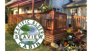 A wooden deck with a railing, a covered porch, and a flower bed with various plants and flowers. - Peaceful, Fully Equipped Cabin Near Beach & Town, Certified NWF Wildlife Habitat (Seaview)