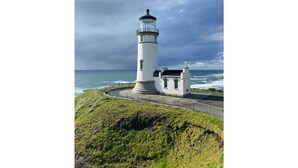 Un phare à l’extérieur blanc et au sommet noir, situé sur une falaise herbeuse surplombant l’océan.