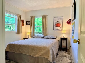 A bedroom with a large bed, two bedside lamps, a framed picture on the wall, and a window with curtains. - Peaceful, Fully Equipped Cabin Near Beach & Town, Certified NWF Wildlife Habitat (Seaview)