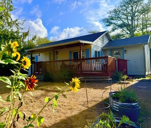 A two-story house with a porch, a small shed, and a garden with sunflowers. - Peaceful, Fully Equipped Cabin Near Beach & Town, Certified NWF Wildlife Habitat (Seaview)