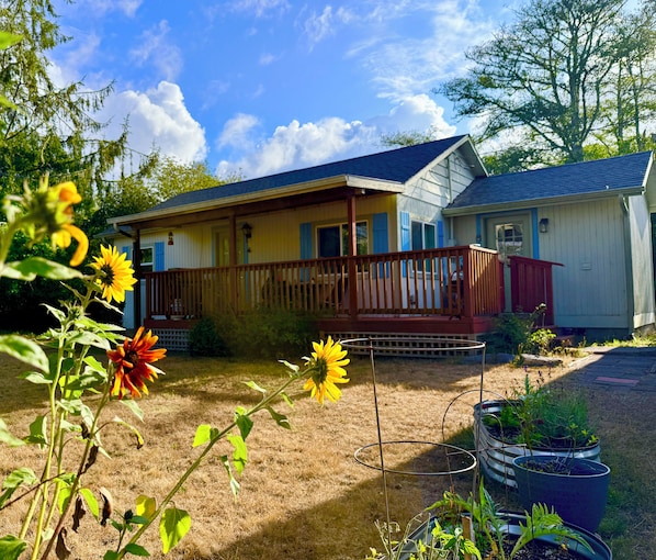 A two-story house with a porch, a small shed, and a garden with sunflowers.