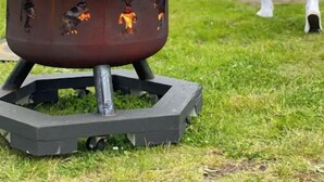 A portable fire pit with flames, a grassy lawn, a wooden deck, and a house in the background. - Peaceful, Fully Equipped Cabin Near Beach & Town, Certified NWF Wildlife Habitat (Seaview)
