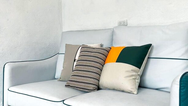 Un canapé blanc orné de motifs turquoise et dorés, deux coussins à motifs et un tapis à poils longs marron.