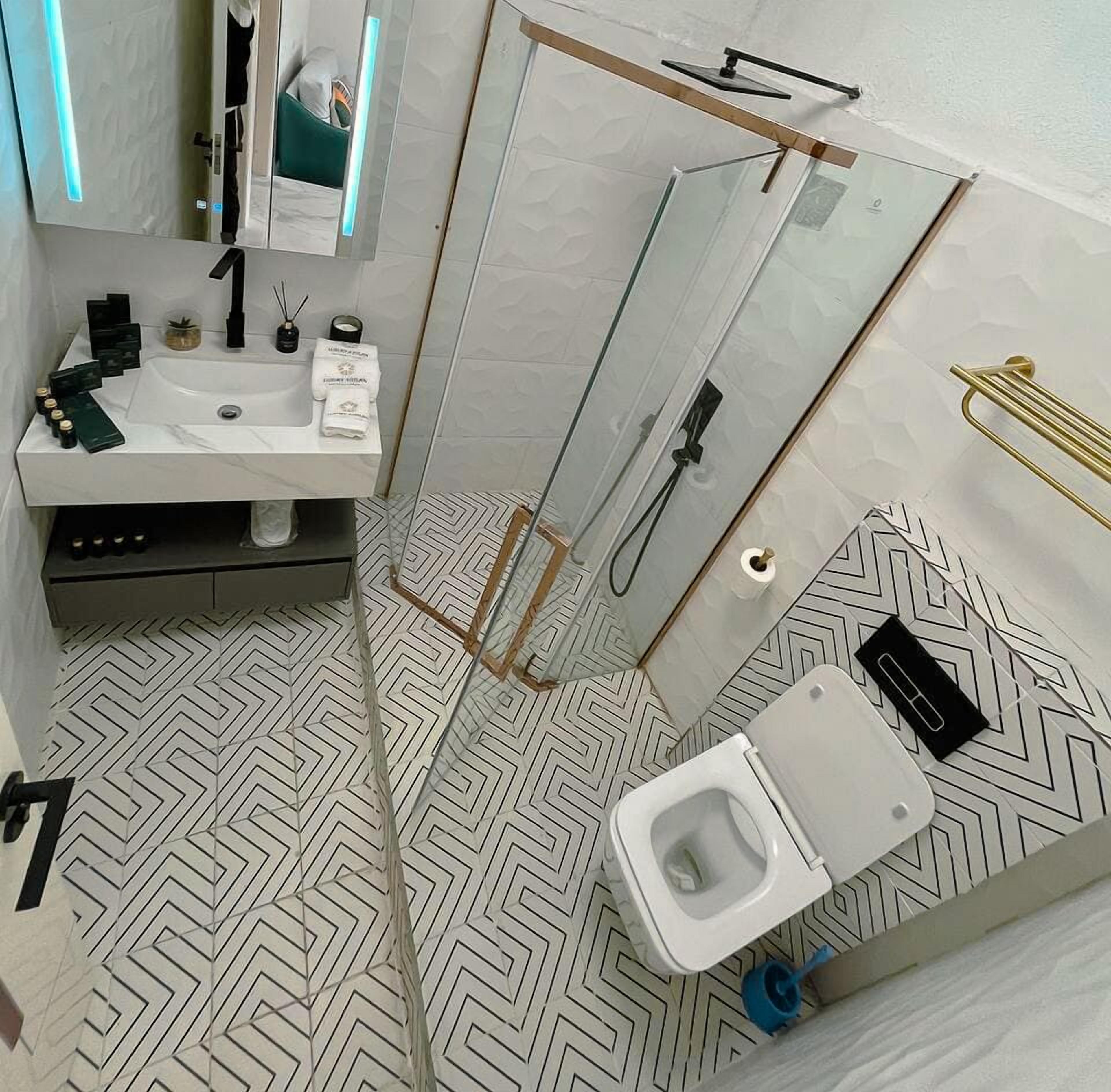 Une salle de bain moderne avec une douche à parois de verre, un lavabo blanc agrémenté d’articles de toilette et un carrelage au motif original.