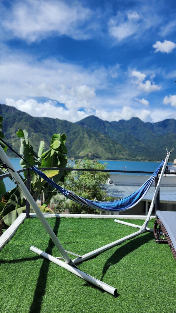 A hammock on artificial grass with a view of mountains and a lake.