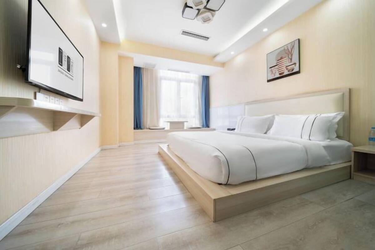 Ein modernes Hotelzimmer mit einem großen Bett, einem flachbildfernseher an der Wand und einem Fenster mit Vorhängen.