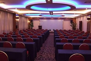 Een vergaderzaal met rijen tafels en stoelen, een spreekgestalte en een podium.