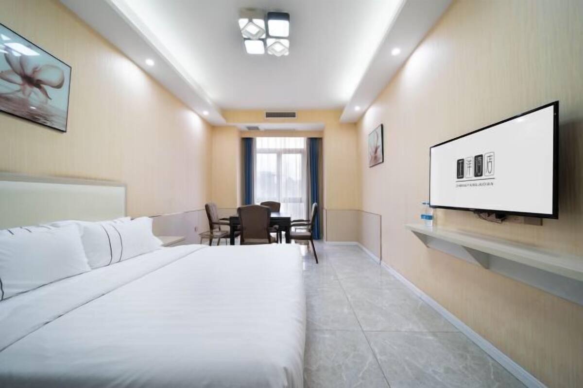 Ein Hotelzimmer mit einem großen Bett, einem Schreibtisch mit Stühlen, einem an der Wand befestigten Fernseher und einem Fenster mit Vorhängen.