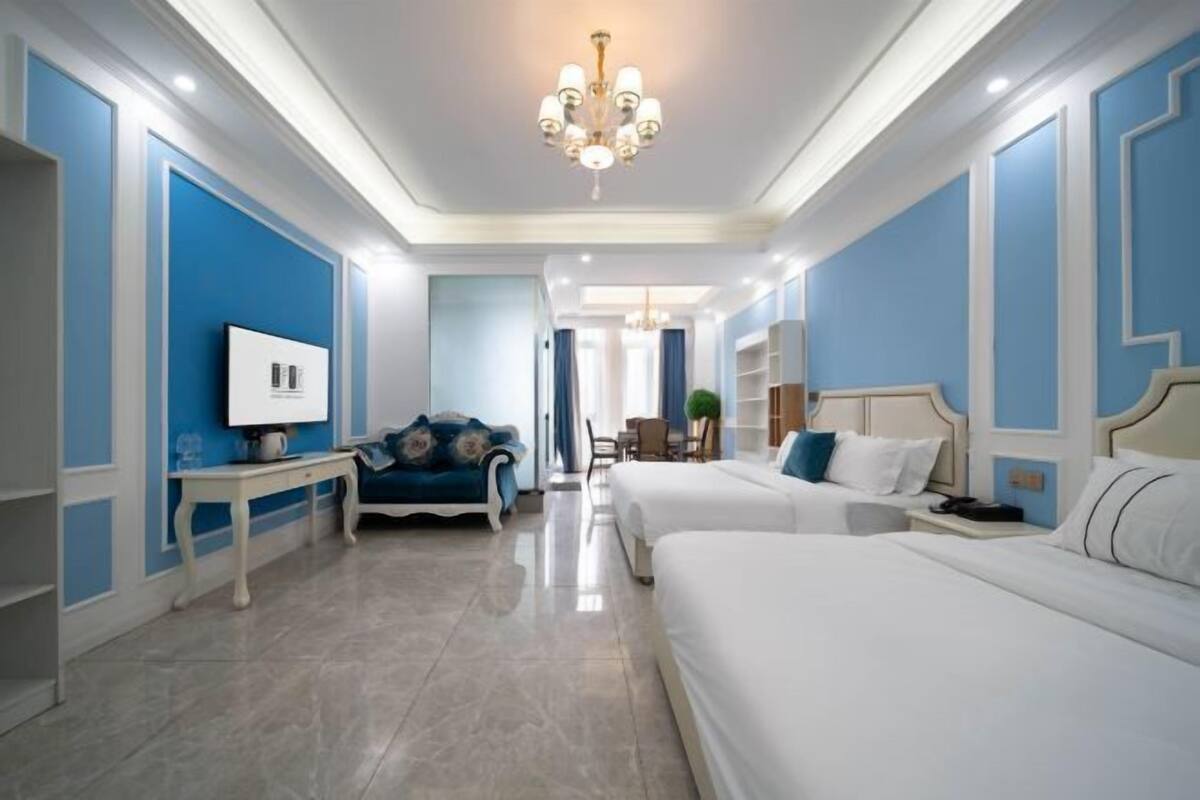 Ein Hotelzimmer mit zwei Betten, einem Fernseher, einem Schreibtisch und einer Kristallleuchter.
