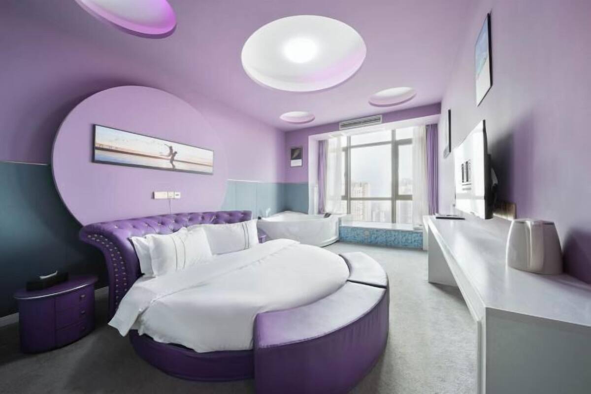 Ein modernes Schlafzimmer mit einem gewölbten Bett, einem Schminktisch mit Spiegel und einem großen Fenster mit Blick auf die Stadt.