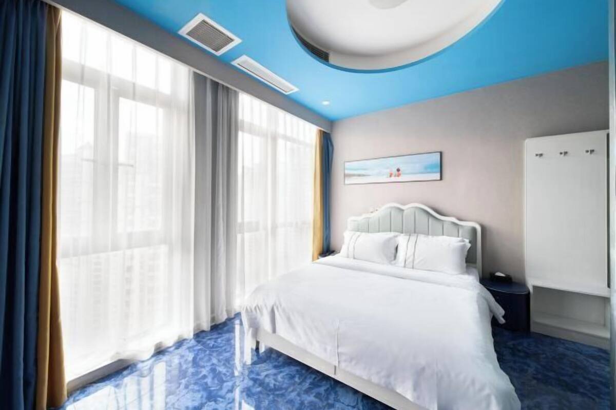 Ein Hotelzimmer mit einem Bett, einem Kleiderschrank, einem Nachttisch und einem großen Fenster mit Vorhängen.