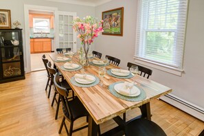 A dining room with a wooden table set for six, surrounded by chairs, with a vase of flowers on the table.