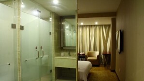 Camera d'albergo con cabina doccia in vetro, un letto, una sedia, una scrivania e una televisione.