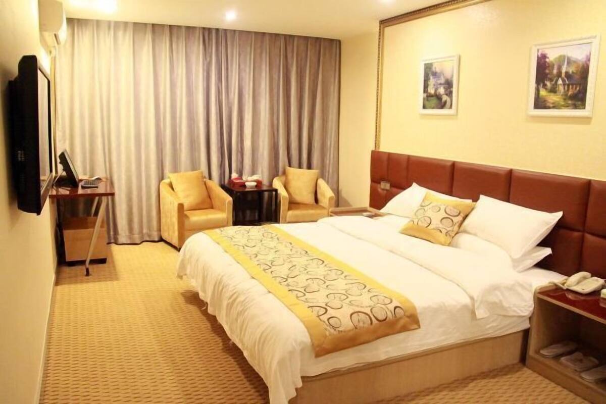 A hotel room with a large bed, a desk with a computer, two armchairs, a TV, and a telephone.
