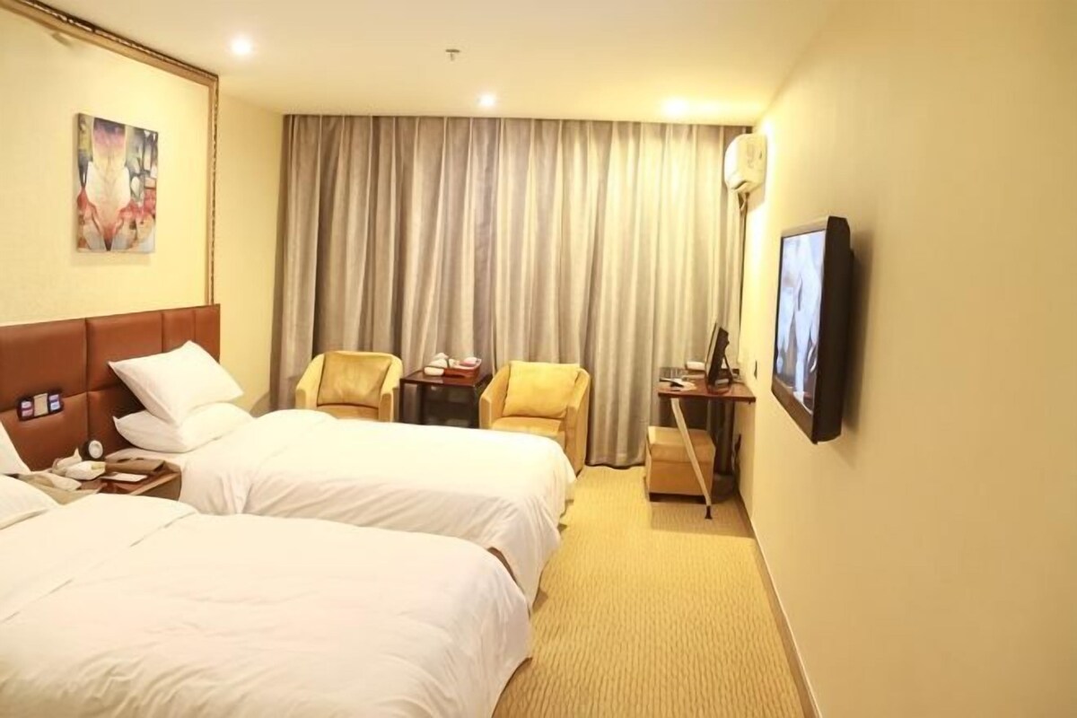 A hotel room with two beds, a desk, a chair, a TV, and a large window with curtains.