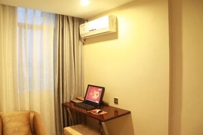 Habitación de hotel con escritorio, ordenador portátil, aire acondicionado y ventana con cortinas.