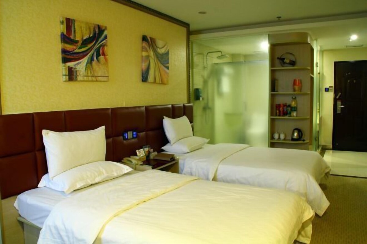 A hotel room with two beds, a headboard, artwork on the wall, a shower area, and a shelf with toiletries.