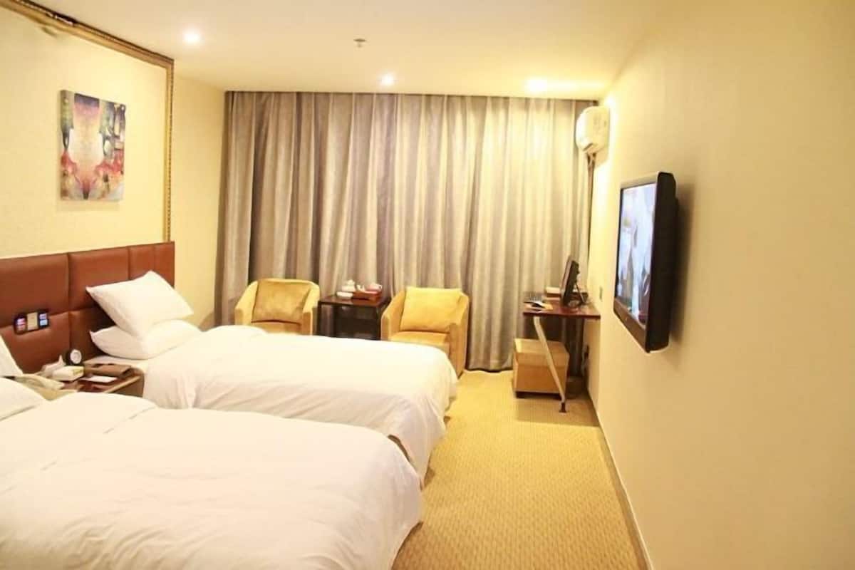 A hotel room with two beds, a desk, a chair, a television, and a large window with curtains.