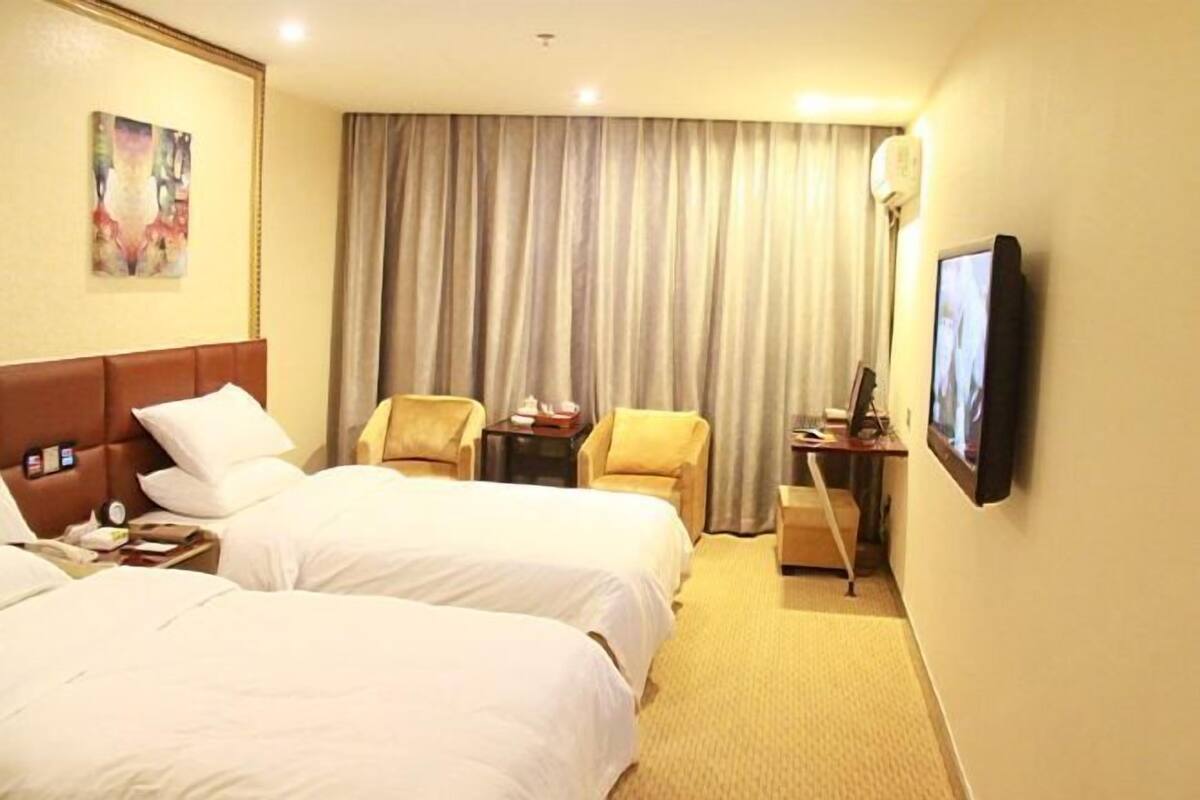 A hotel room with two beds, a desk with a computer, a chair, and a television on the wall.