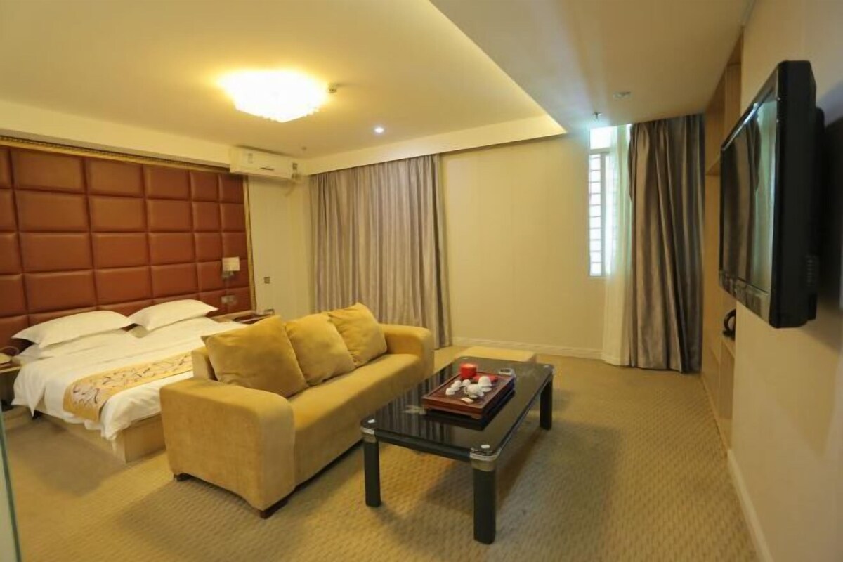 Una habitación de hotel con cama, sofá, mesa de centro, televisor y cortinas.
