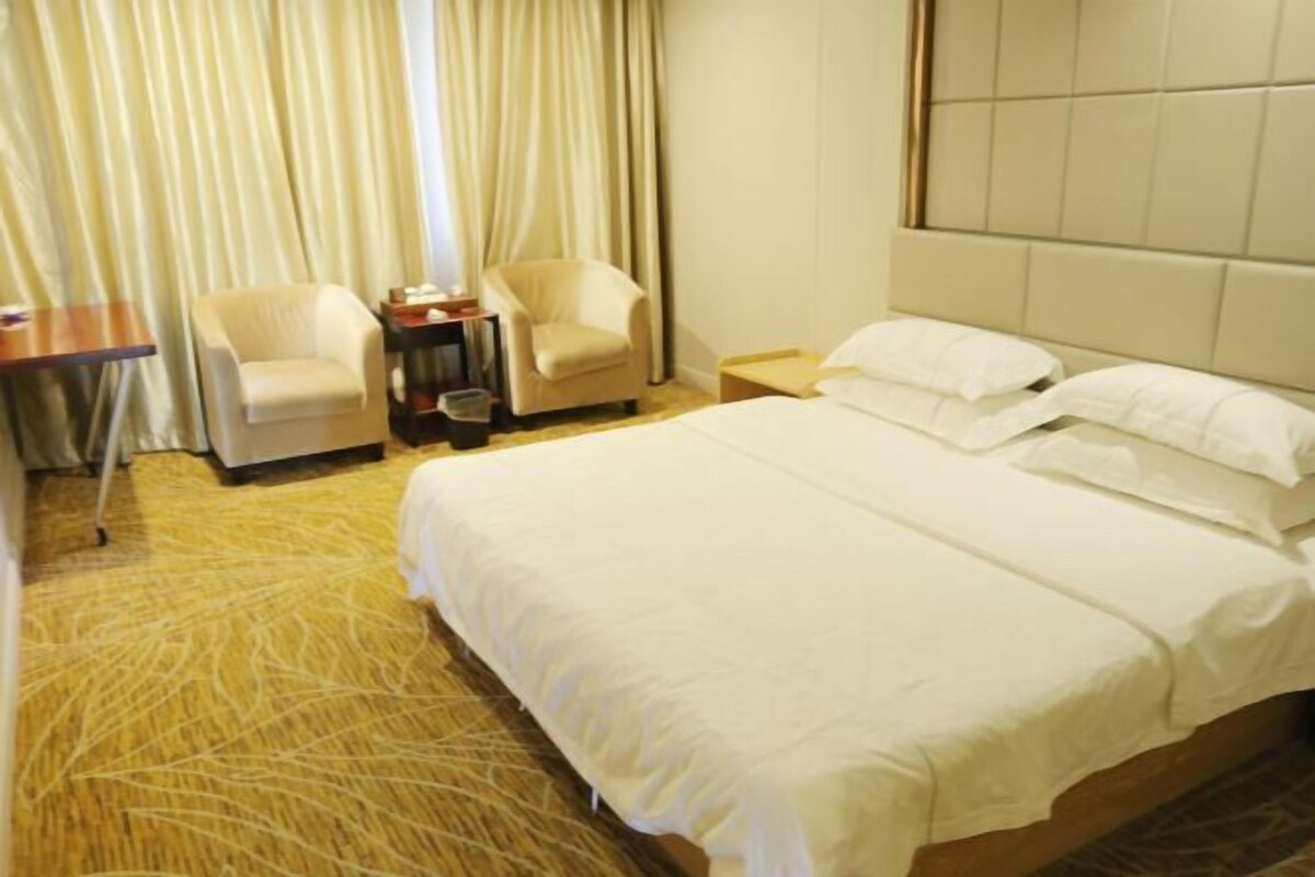 Una habitación de hotel con una cama grande, dos sillas, una mesita y una ventana con cortinas.