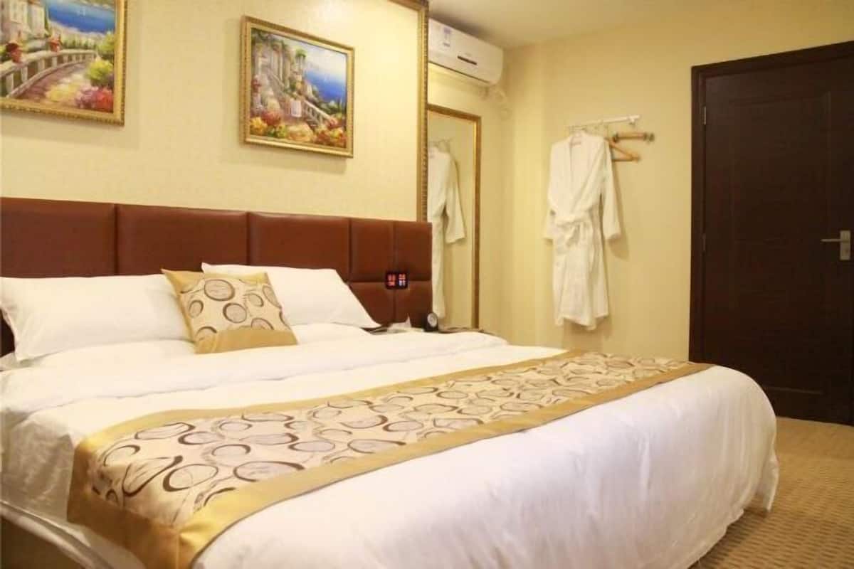 A hotel room with a large bed, a headboard, a painting on the wall, and a door.