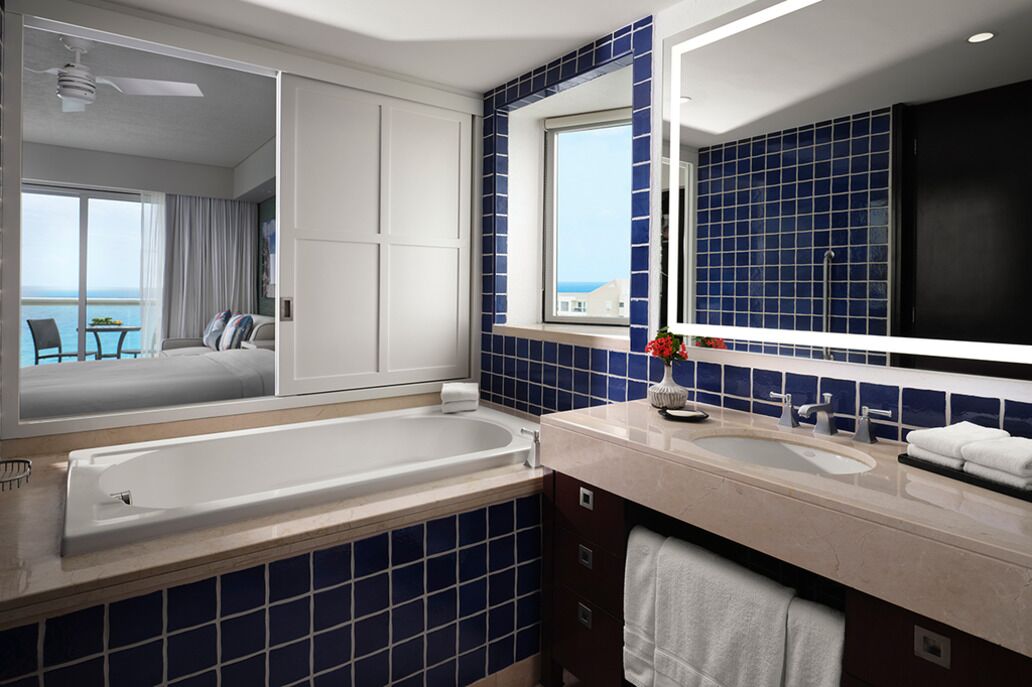 A modern bathroom with a large bathtub, a vanity with a mirror, and a view of the sea through a window.