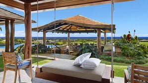 A wooden swing chair and a cushioned bench with pillows, overlooking a pool and lush garden. - Panoramic Ocean Views From Private Gated Estate (Kaloa)