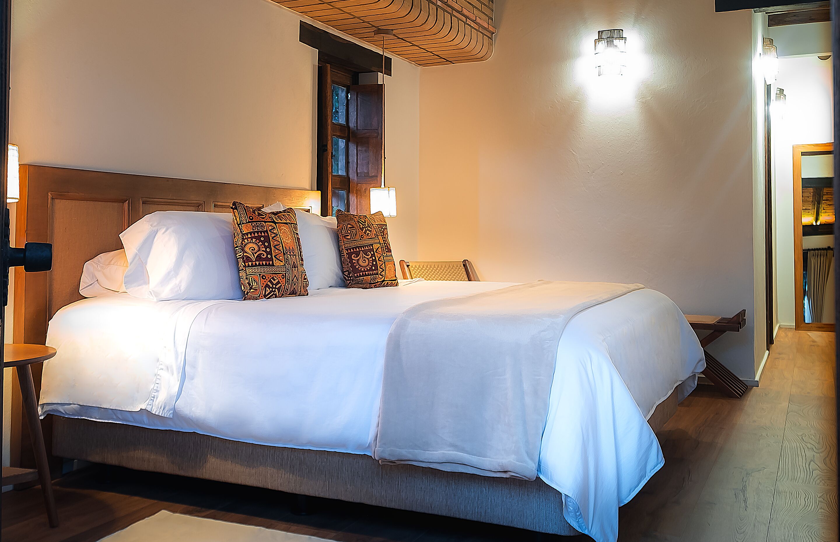 A neatly made bed with white linens and patterned pillows, a wooden headboard, and a small bedside table with a lamp.