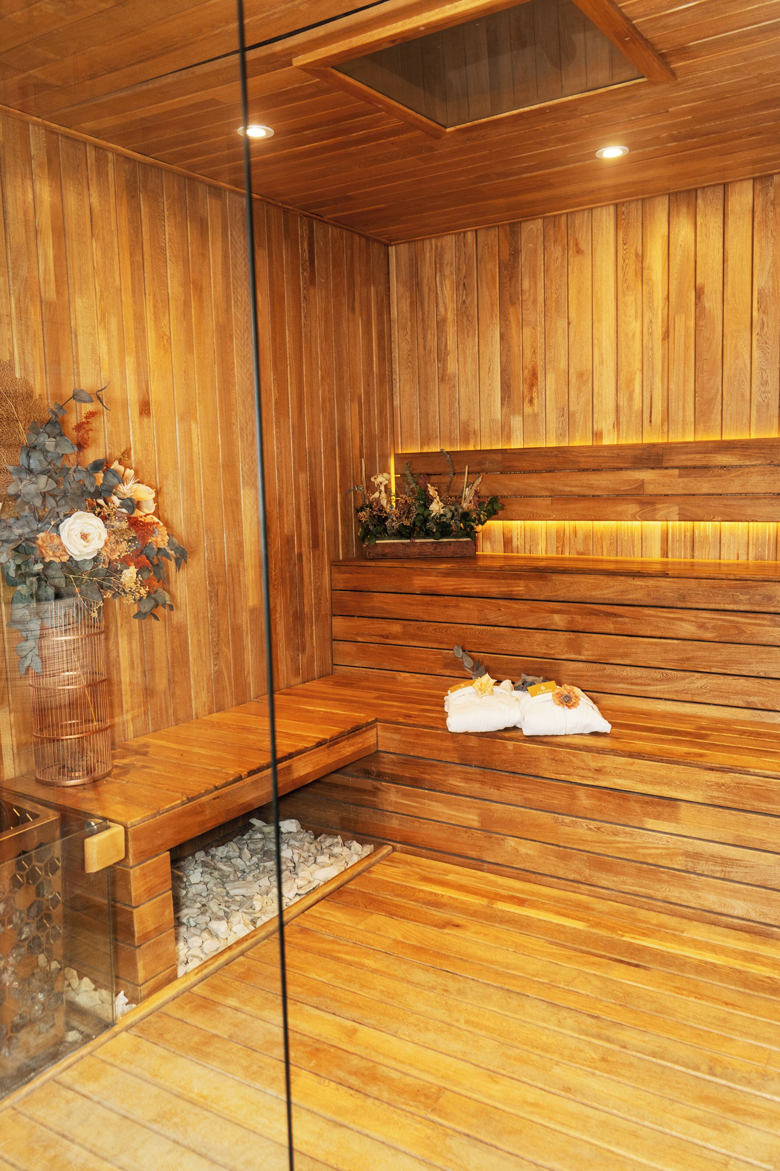 A wooden spa room with a bench, a small table with flowers, and a glass partition.
