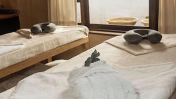 Una habitación con dos camas, cada una con una almohada y una toalla enrollada. Hay una ventana con cortinas y vistas al exterior.