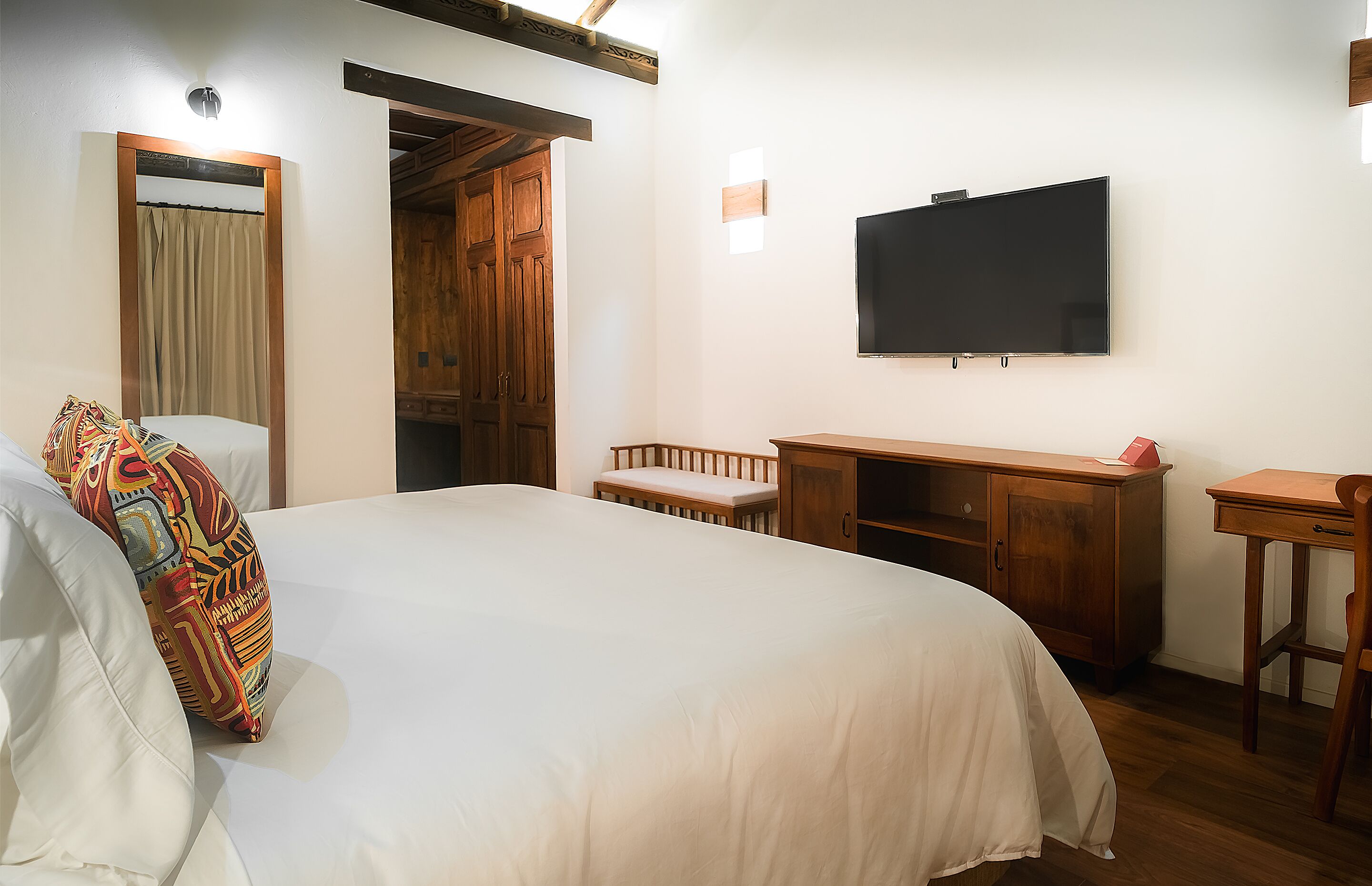 A bedroom with a large bed, a wooden desk, a television, and a wardrobe.