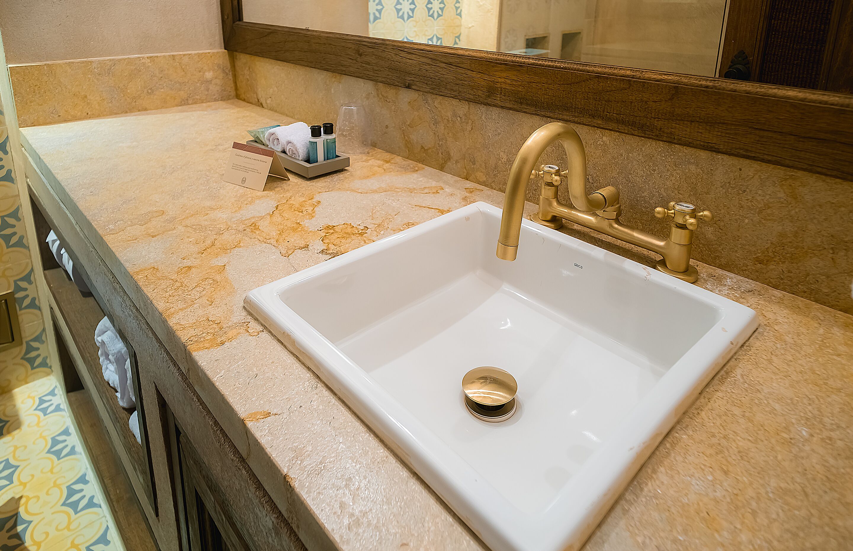 A bathroom with a white sink, gold faucet, and a mirror above it.