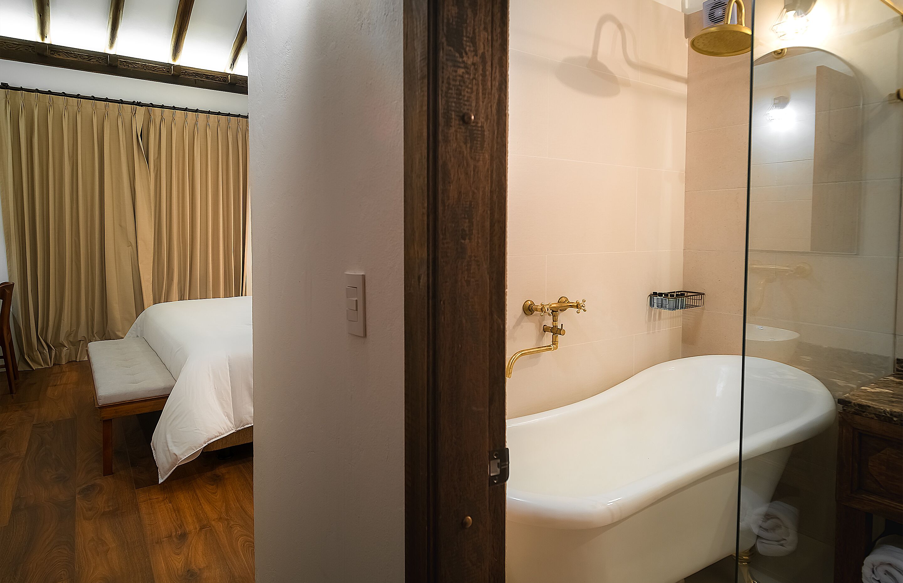 A bedroom with a bed, a wooden floor, and a bathroom with a bathtub and a shower.