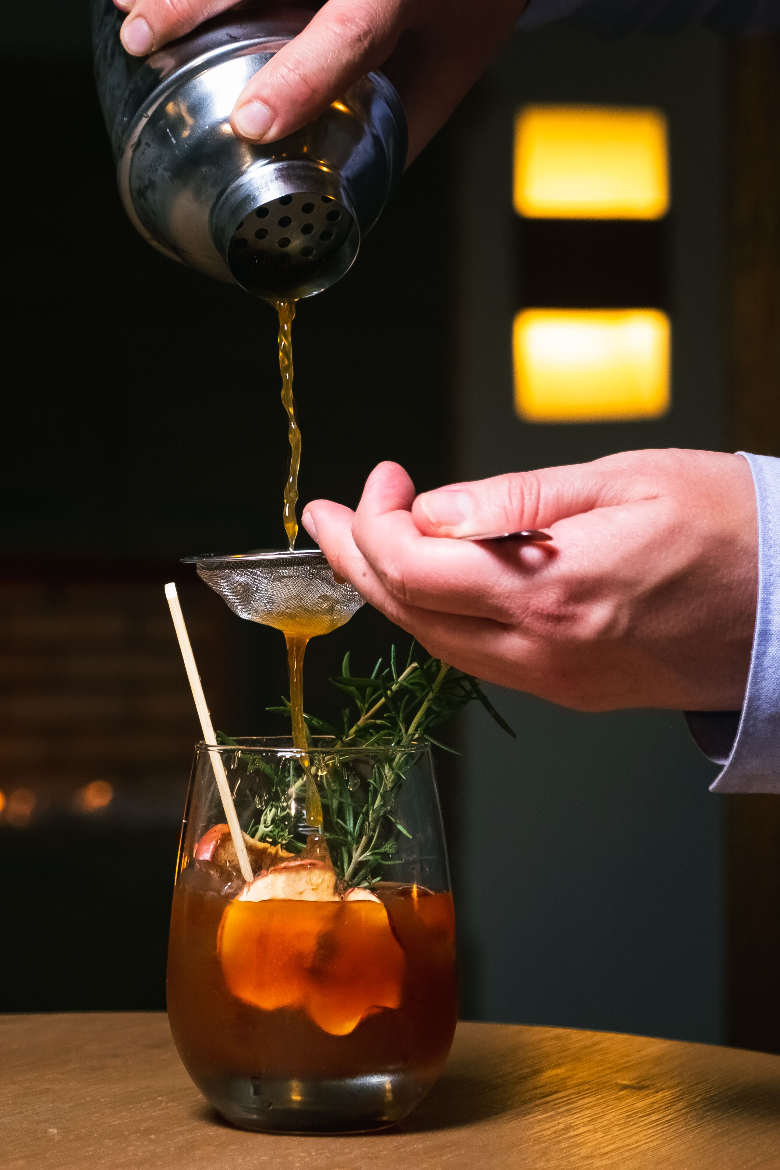 A person pouring a drink from a shaker into a glass with a straw and garnish.