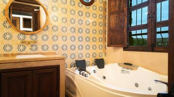 Un baño con una bañera grande, armarios de madera, un espejo redondo y papel tapiz estampado.